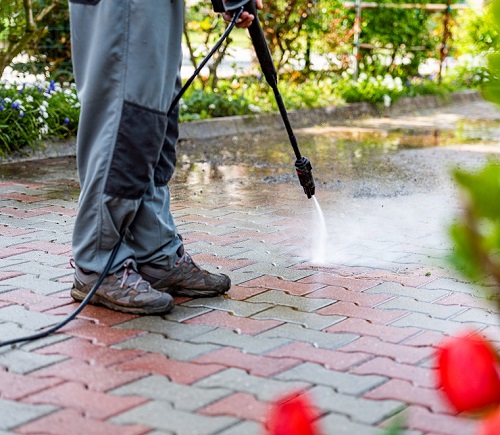 man pressure washing pavers in driveway